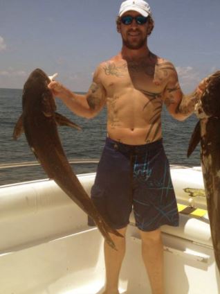Chase Landry on a boat holding fish and displaying his tattoos.